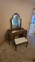 Front view of vintage Malcolm wooden dressing table with attached mirror and matching bench in room setting.