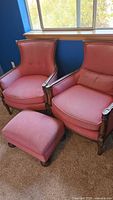 Set of two pink fabric armchairs and one matching ottoman showing full set from side angle in room lighting.