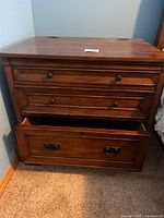 Front view of wooden file drawer with three drawers, showing drawer knobs and lower metal handles.