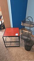 Full view of the wood top metal table, tiered basket unit, and wastebasket on carpeted floor against blue wall