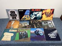 Front display of 12 vinyl record albums in original sleeves featuring a variety of artists and genres, arranged in two rows of six on a light surface.
