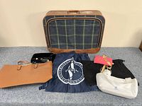 Full view of all 7 bags including vintage suitcase and assorted totes and small bags on a grey surface in front of a beige wall