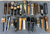 Top-down view of the entire lot showing 20 unique beer tap handles arranged on a grey surface.