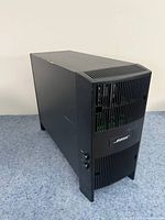 Black rectangular Bose Acoustimass 6 III subwoofer standing on a carpeted surface, front and side vents visible with control knobs on the side panel.