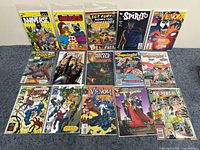 Photo showing a variety of comics including The Aniverse, Venom, Sgt. Fury, The Spirit, Spider-Man, and Supergirl arranged in three rows on a blue surface.
