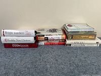 Full view of the 12 cookbooks laid on carpet showing spines and titles.