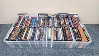 Photo showing the full plastic bin filled with DVDs and Blu-Rays organized standing upright facing front with visible spines.
