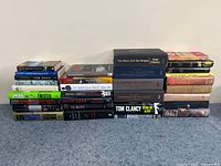 Stack of fiction books showing various titles and authors including Tom Clancy, Ken Follett, Jonathan Kellerman, and others.
