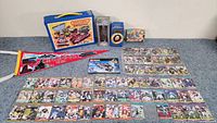 Photo of 62 football cards arranged on table along with Matchbox carrying case, Cincinnati pennant, Duck Dynasty bobblehead, Lord of the Rings goblets, vintage puzzle box top and Lego instructions.