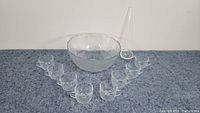 Full set including punch bowl, 8 glass cups arranged in front of the bowl, and plastic ladle standing behind the bowl.