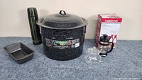 Photo showing all items: large granite speckled canner with lid, green metal water bottle, small loaf pan, black French press, and clear glass teapot.