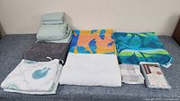 Full lot laid out on bed showing sheet set folded on the left, bath rug in front, bath towels including two colorful sea-themed towels, one white towel, hand towel in checkered pattern, unopened pillowcase set, and two seashell pillow covers on the right.