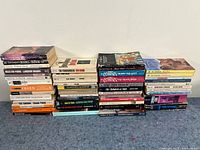 Wide view showing four stacks of paperback books by multiple authors in used condition
