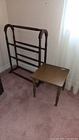 Photo of wooden blanket rack and small side table together on carpeted floor near window.