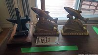 Photo showing set of cast iron anvil, hammer on wooden base, and two gold-painted Newfoundland fish bookends