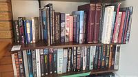 Books arranged on wooden shelves in a home library setting, showing a variety of titles from fiction and historical genres.