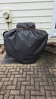 Broil King propane grill covered with a black protective cover, secured with an orange strap.