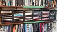 Shelf view showing multiple CDs placed in standard jewel cases, showing a variety of musical genres and artists, including Eric Clapton, Johnny Cash, Alan Bennett, and classical opera.