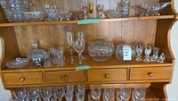 Wooden hutch with mixed crystal and glassware items including bowls, wine glasses, small glasses, a lidded bowl, and decorative flower frog.