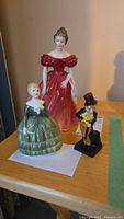 Three Doulton figurines placed on a wooden surface: two female in period dresses and one male in formal attire.