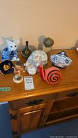 Wide shot of all figurines and trinket items arranged on wooden surface showing cat, birds, snail, boy figurine, trinket dish, and lidded bowl