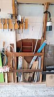 Garden tools hung on wooden rack including rake, shovel, hand tools, garden umbrella and candy cane decoration.