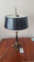 Front view of vintage brass and black table lamp with black drum shade on wooden surface.