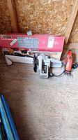 Mastercraft MC2000 electric chainsaw with blade guard and Black & Decker electric clippers placed on wooden surface with original box in the background.