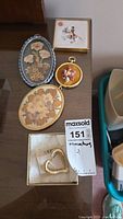 Top-down photo showing four framed miniatures with various floral and whimsical designs, heart pin in open box with tag on table