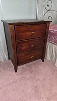 Side view of one wooden nightstand showing three drawers with metal handles and dark finish