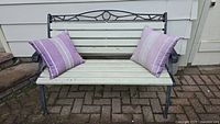 Full view of the metal and wood patio bench with two purple striped pillows placed on it, showing the bench design and condition.