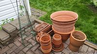 Overview of clay and plastic pots stacked on paved area with green grass background. Includes tomato cages.