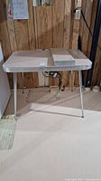 Vintage metal table with beige laminate top and two leaves, set up in basement with wood panel walls.