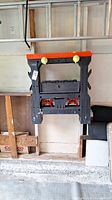Folded black plastic sawhorse with orange top hanging on wall.