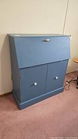 Blue painted wooden secretary desk closed, showing two lower cabinet doors with white knobs.