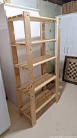 Front view of a five-shelf wooden utility shelving unit in a basement, showing light-colored unfinished wood construction.