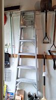 Full frontal view of aluminum step ladder showing full height and structure against wall with adjacent tools.