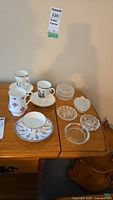 Overview of porcelain teacups, saucers, and glass containers arranged on wood surface
