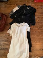 Six dresses laid out on hardwood floor including one white embellished dress, black dresses, and a beige floral dress.