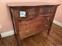 Front and side view of the antique wooden dresser showing brass handles and curved legs.