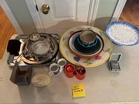 Items arranged on table showing plates, bowls, cups, candle holders, metal trays and serving pieces