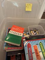 Photo showing a large clear plastic bin filled with various educational books and instructional materials including a Berlitz Self-Teacher Italian guide.