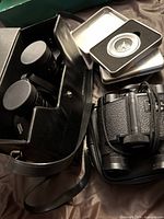 Bushnell binoculars in black carrying case with lens covers visible, compass in metal tin case beside them