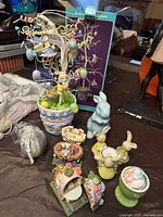 Multiple ceramic and plastic Easter figurines and a decorative Easter tree in a pastel pot on a tabletop.