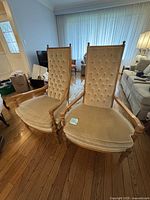 Front view of two matching vintage armchairs with beige tufted backs and wooden frames in a living room.