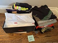 Photo of clothing and footwear lot showing folded T-shirts and pants stacked, and a Levi's shoebox with shoes inside.