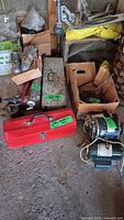 Photo showing collection of assorted hand tools including red and steel toolboxes, hand tools such as wrenches, ratchet, wires, and three electric motors on a concrete floor.