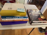 Wide shot showing six stacked cookbooks and one separate book on table.