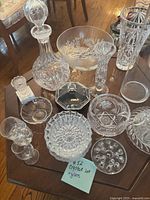 Photo showing the entire crystal and glassware set on a wooden table with 13 pieces including decanter, etched bowls, glasses, vase, and dishes.