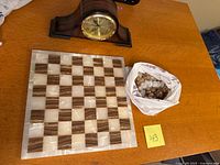 Marble chessboard with alternating brown and white squares next to traditional mantel clock and bag of chess pieces.